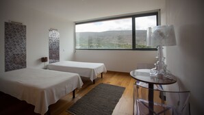 A hotel room with two beds, a large window with a mountain view, a table with a lamp, and patterned wall decor. - HI Alvados - Pousada de Juventude - Hostel (Porto de Mos)