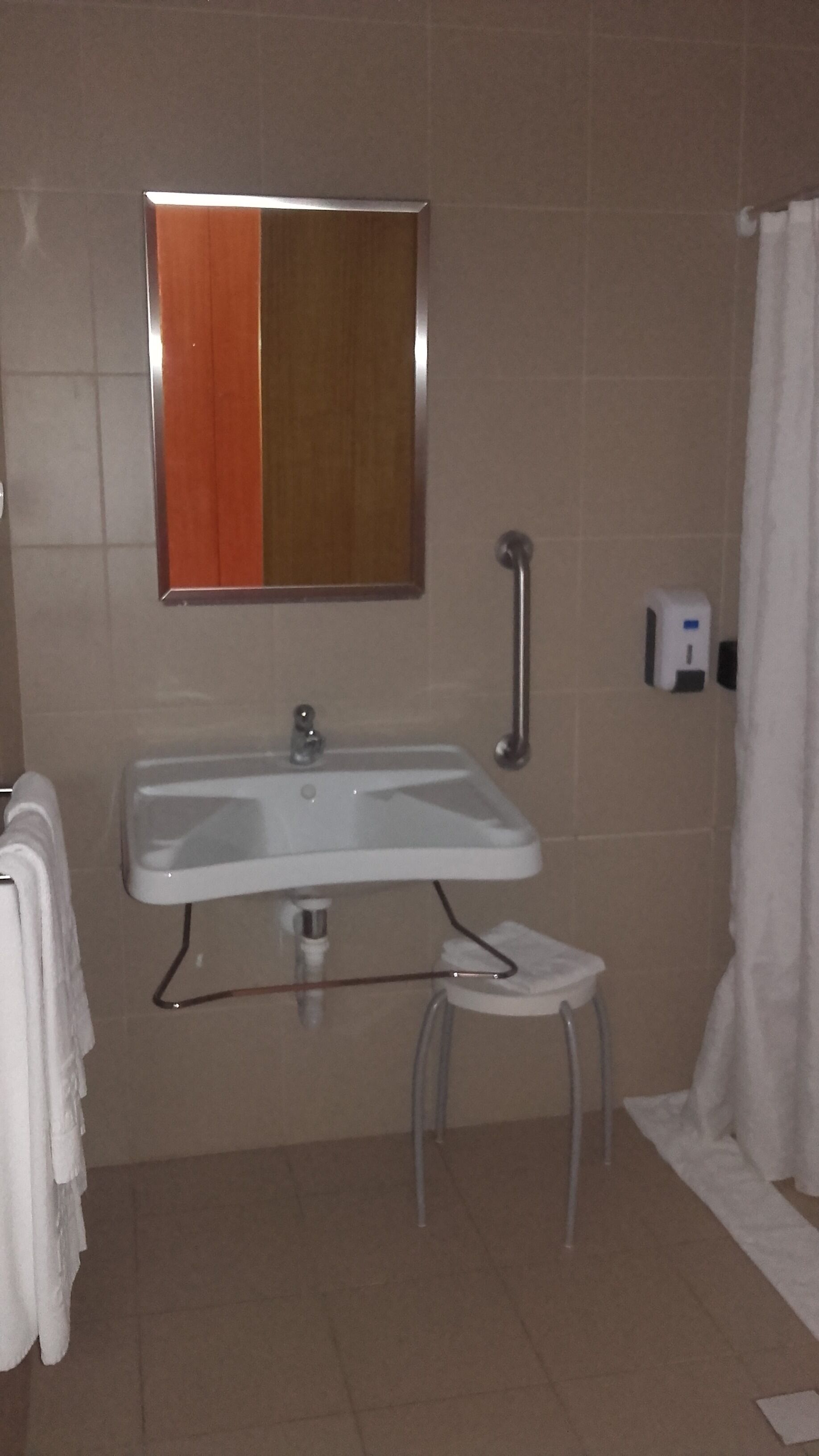 Une salle de bain avec un lavabo blanc, un miroir, un porte-serviettes, un sèche-mains et un rideau de douche.