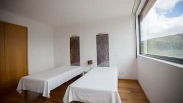 Una habitación con dos camas individuales, un armario de madera, una mesita con lámpara y una ventana con vistas a un paisaje montañoso.