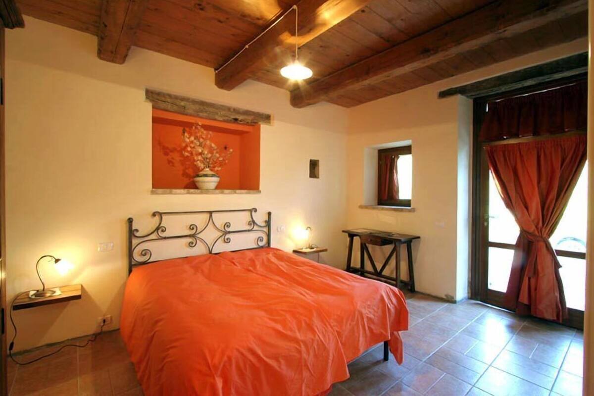 Une chambre à coucher avec un lit, des lampes de chevet, une fenêtre avec des rideaux et un plafond en bois.