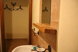 Une salle de bain avec un lavabo blanc, un miroir et une étagère en bois au-dessus du lavabo.