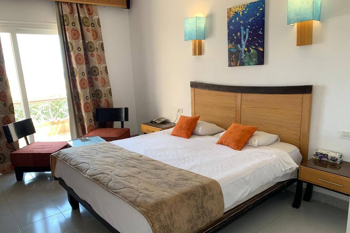 A hotel room with a large bed, two bedside tables, a chair, a desk, and a window with curtains.