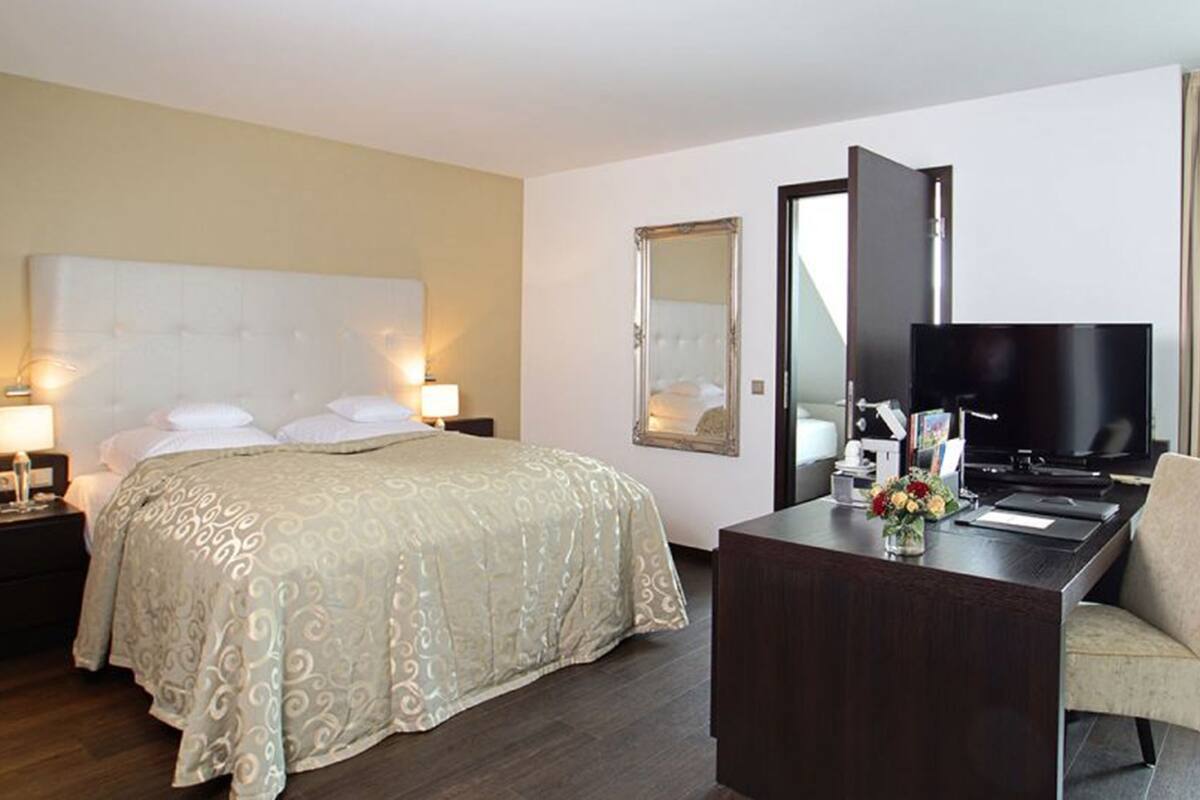 Habitación de hotel con una cama grande, un escritorio con silla, televisor y espejo.