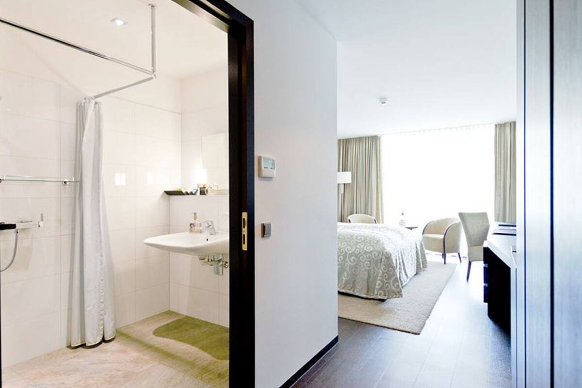 Una habitación de hotel moderna con ducha, lavabo y cama con vista a la ciudad.