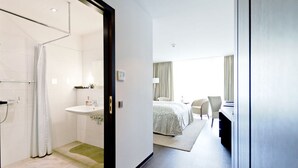A modern hotel room with a shower, sink, and a bed with a view of the city.