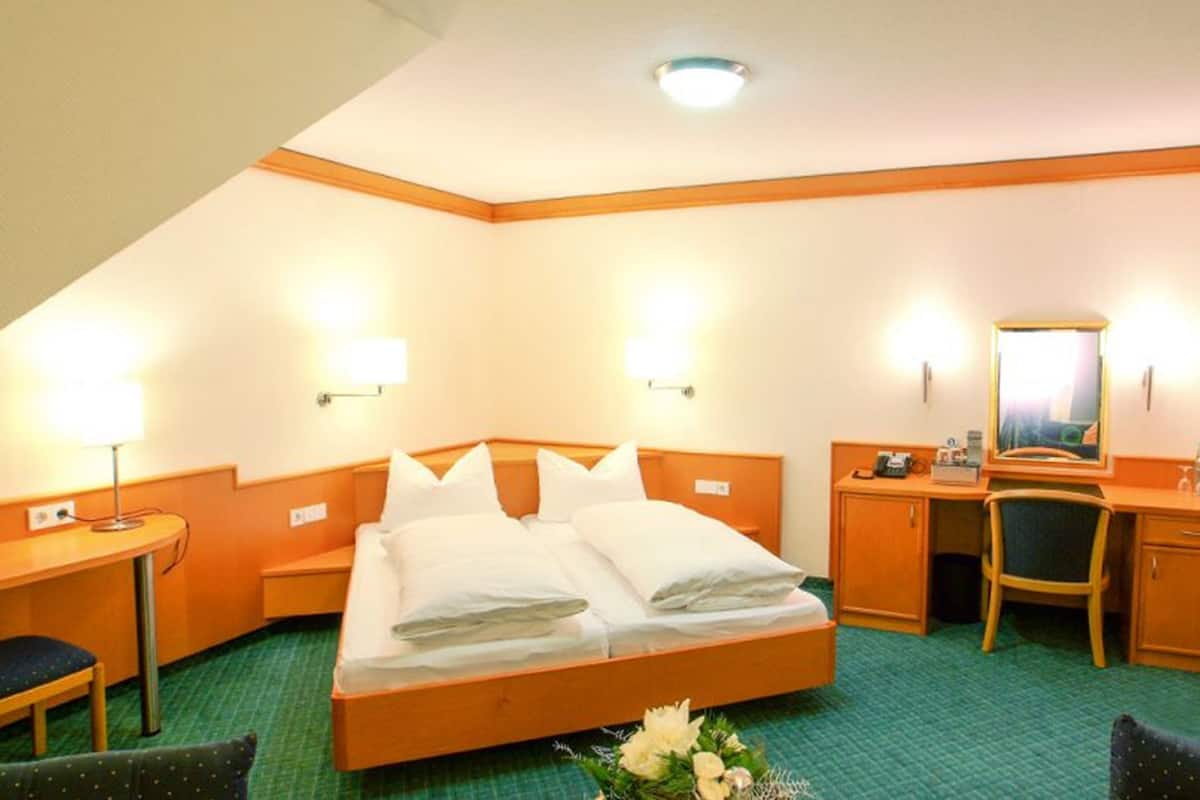 Una habitación de hotel con cama, escritorio, silla, espejo y mesita de noche.