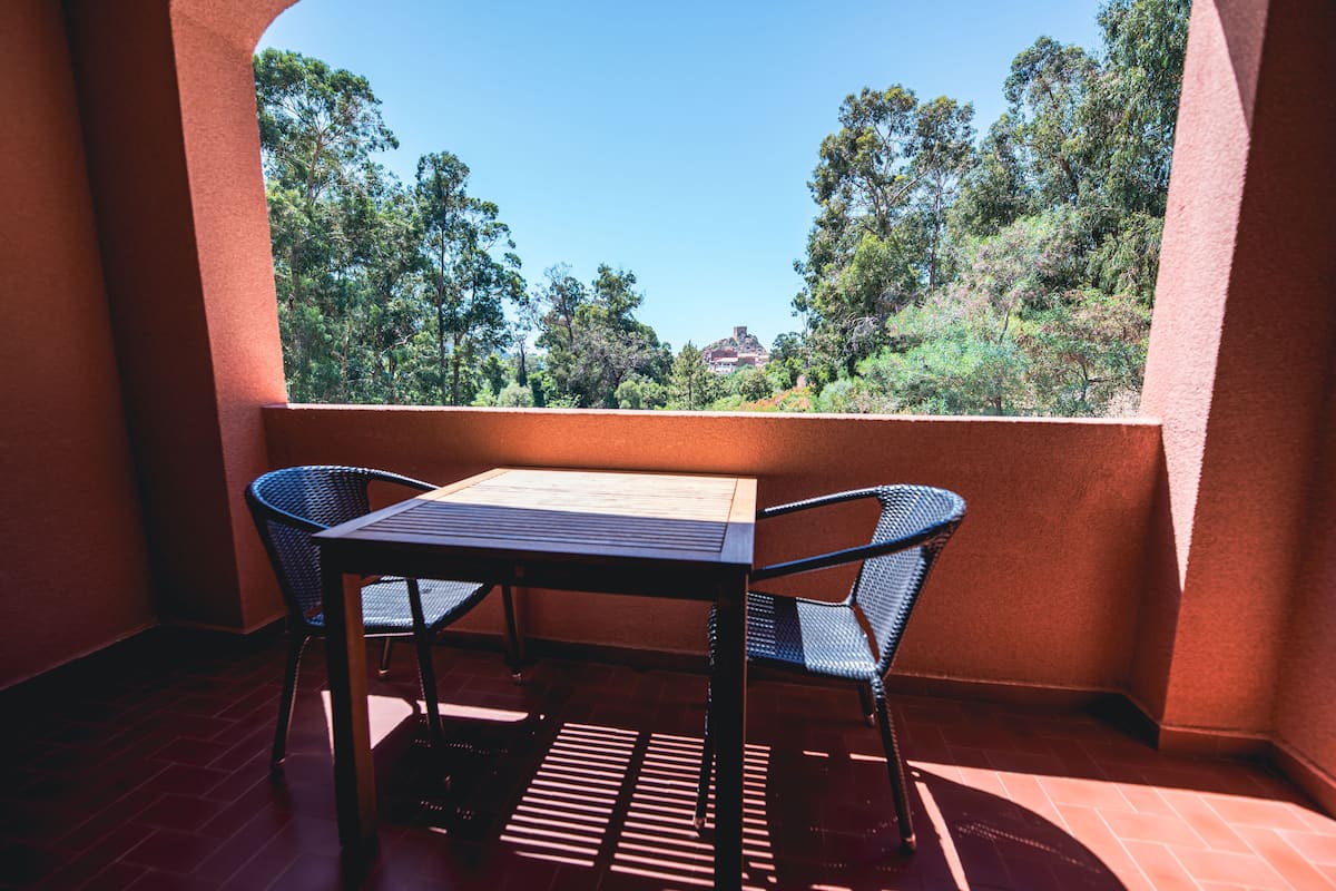A balcony with a table and two chairs, overlooking a forested area.