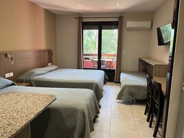 A hotel room with three beds, a desk, a TV, and a balcony with outdoor furniture.