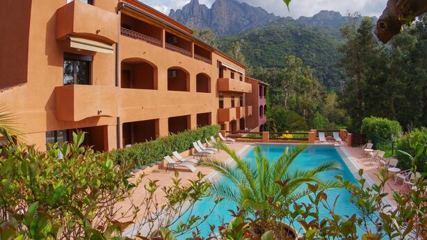Un hotel con piscina, zona de estar al aire libre y montañas al fondo.