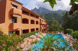 A hotel with a pool, outdoor seating, and a mountainous backdrop. - Hôtel Corsica (Ota)