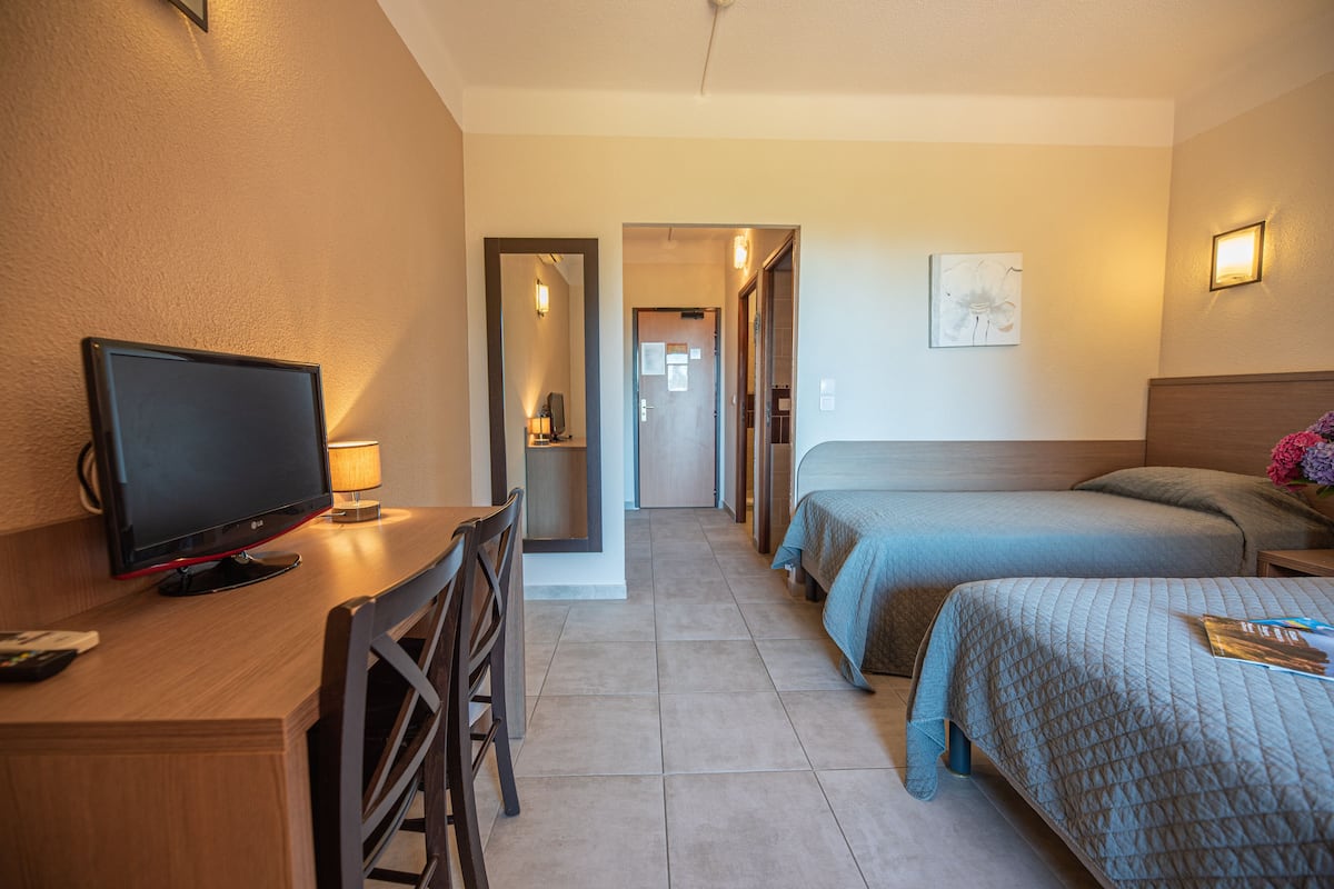 A hotel room with a desk, TV, two beds, a chair, and a bathroom visible through an open door.