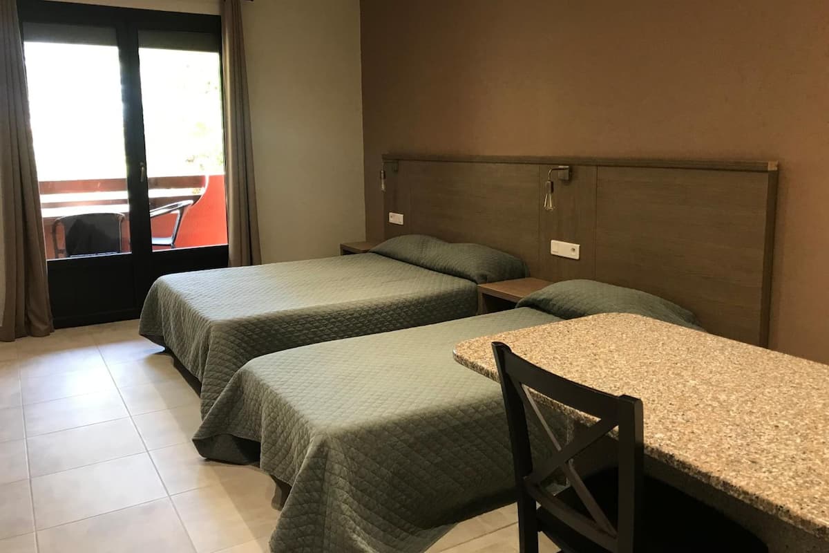 A hotel room with two beds, a small table, and a chair.