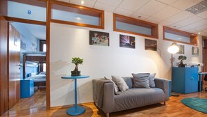 A modern hotel room with a grey sofa, a small round table with a plant, and artwork on the walls. - Hostel Bureau (Zagreb)