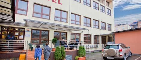 Un hostal con un cartel que dice "HOSTEL" sobre la entrada, zona de estar al aire libre y un coche estacionado.