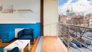 A modern living room with a blue sofa, a white table, and a view of a cityscape with buildings and a church spire. - Hostel Bureau (Zagreb)