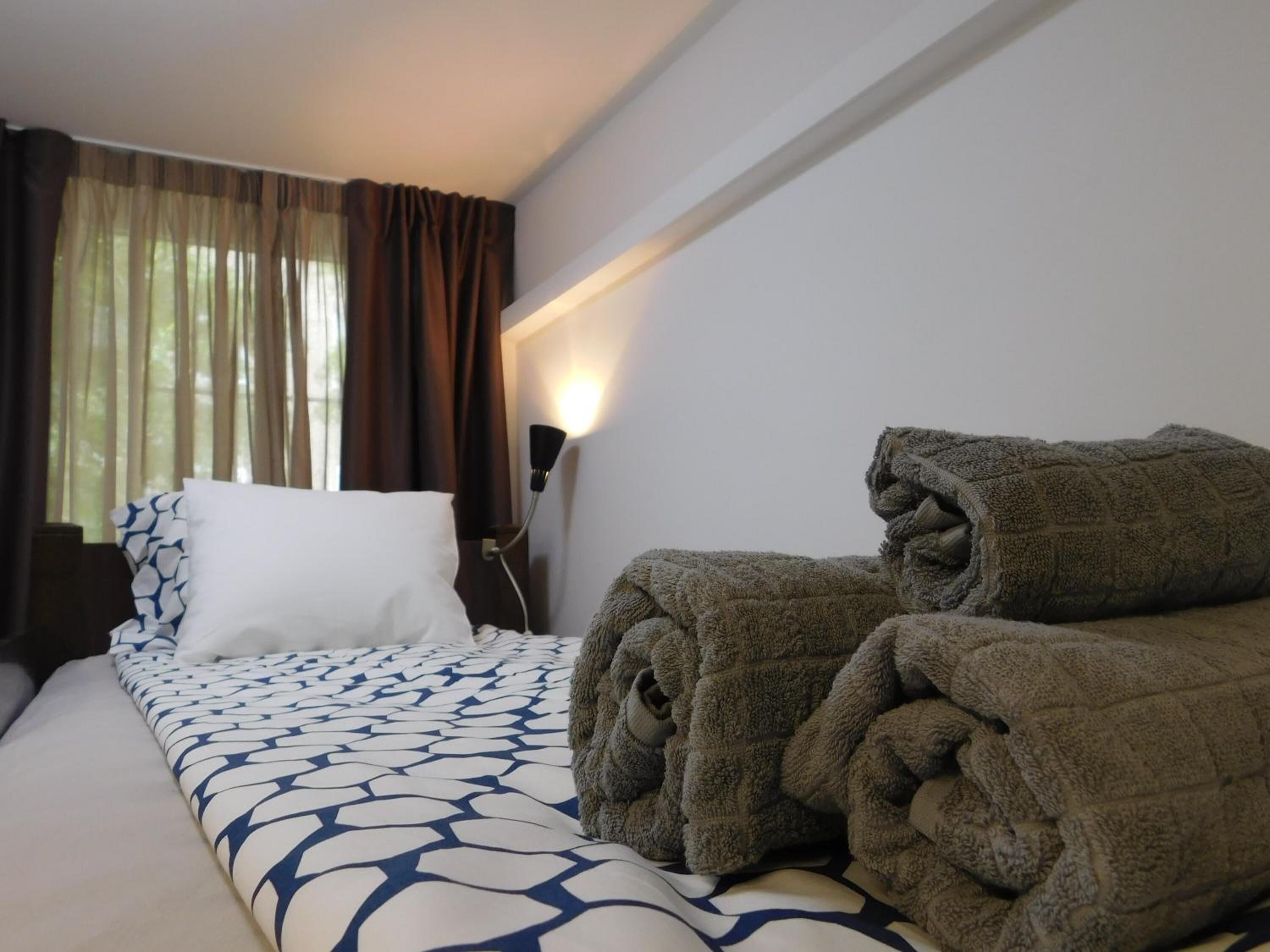 A hotel room with a bed, a nightstand, a lamp, and a window with curtains.