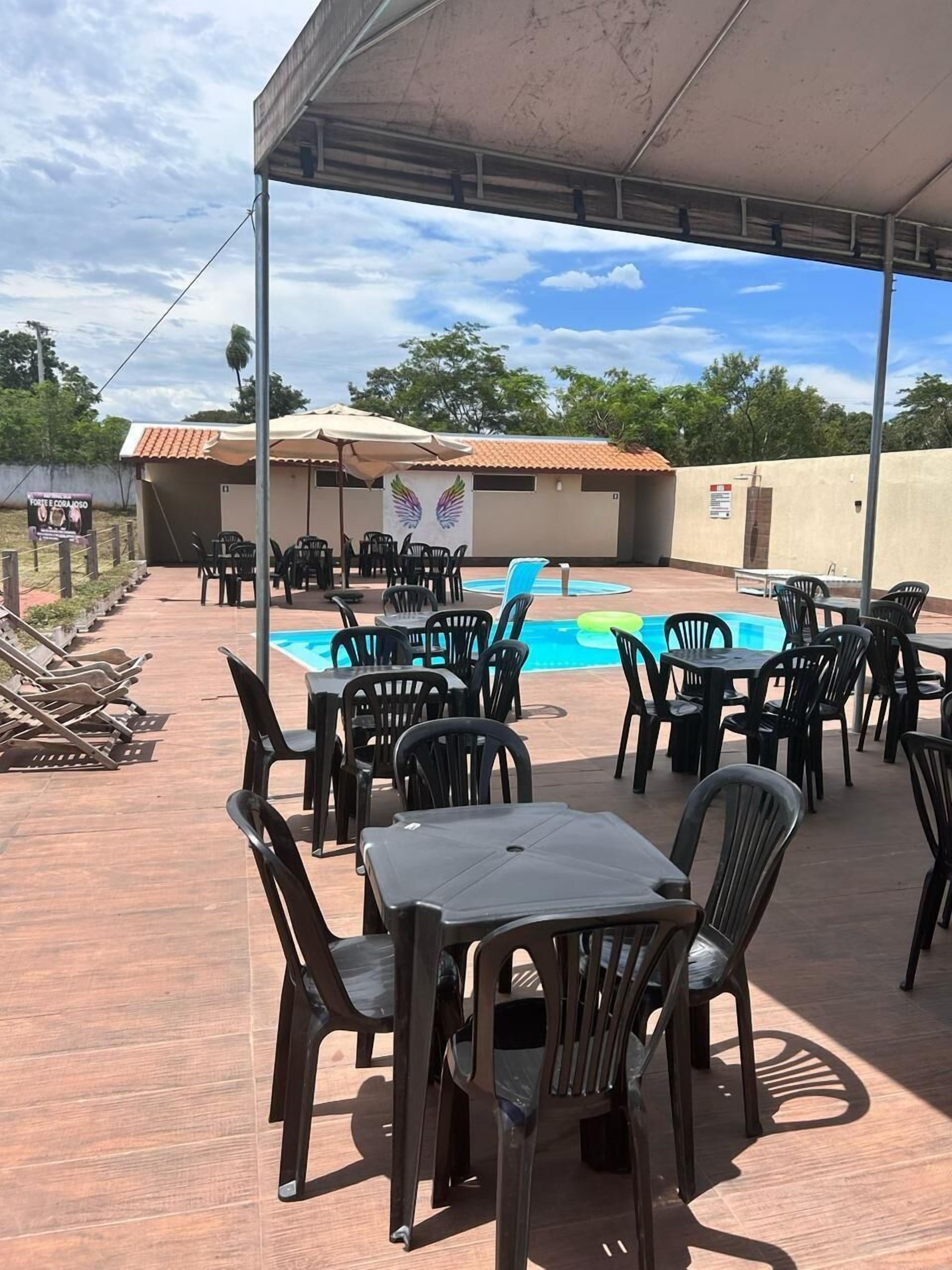 Un patio al aire libre con piscina, rodeado de sillas y mesas de plástico, bajo una zona cubierta.