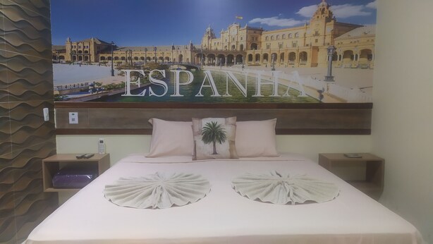 A hotel room with a large bed, two nightstands, a wall-mounted telephone, and a poster of a building with the word "ESPAÑI" on it.