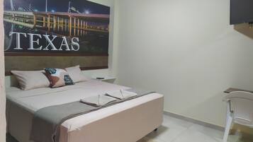 Habitación de hotel con cama, almohadas, mesita de noche, una silla y una pared con un cartel grande que dice 'TEXAS'.