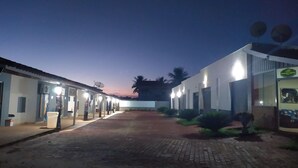 Un patio con un camino pavimentado, edificios con iluminación exterior y un atardecer al fondo.