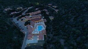 An aerial view of a resort with multiple buildings, a swimming pool, and a parking area surrounded by dense vegetation. - Sosventos Village (Teulada)