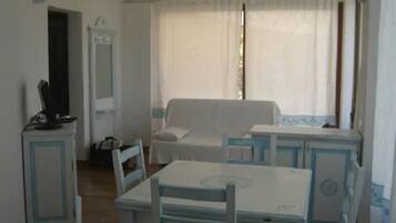 A room with a white sofa, a small table, a chair, and a television on a cabinet.