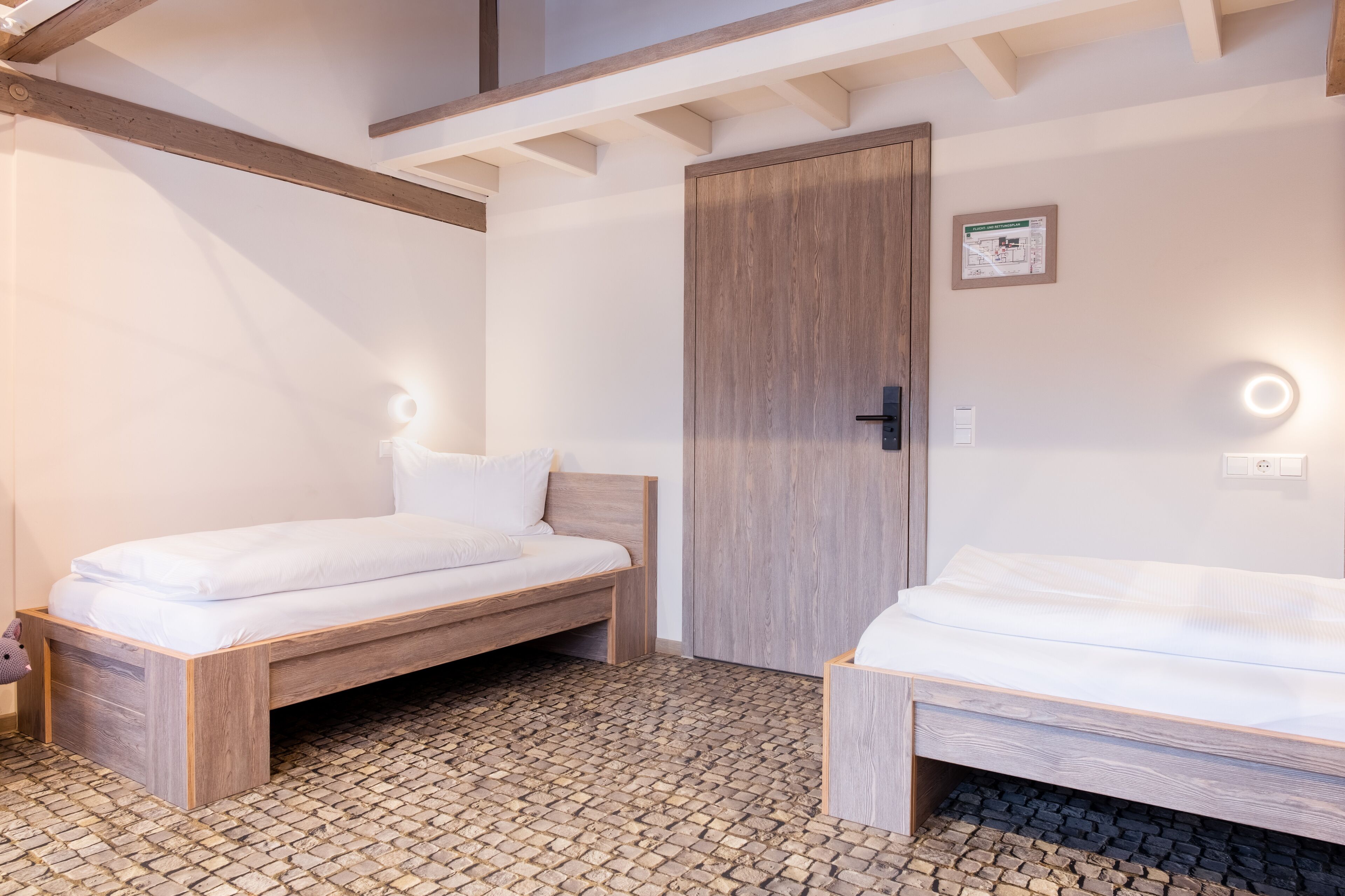 Una habitación con dos camas de madera, una puerta de madera y suelo de adoquines.