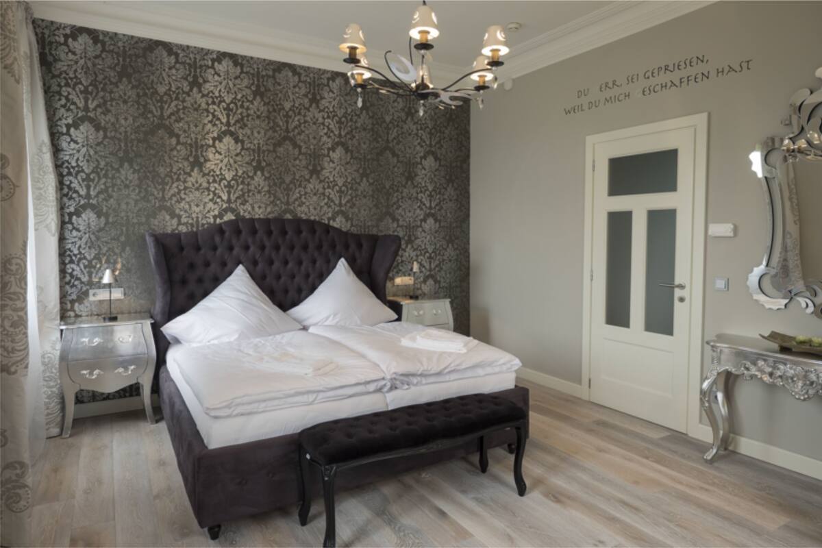Un dormitorio con una cama grande, un banco, una mesita de noche, un aparador y un espejo.
