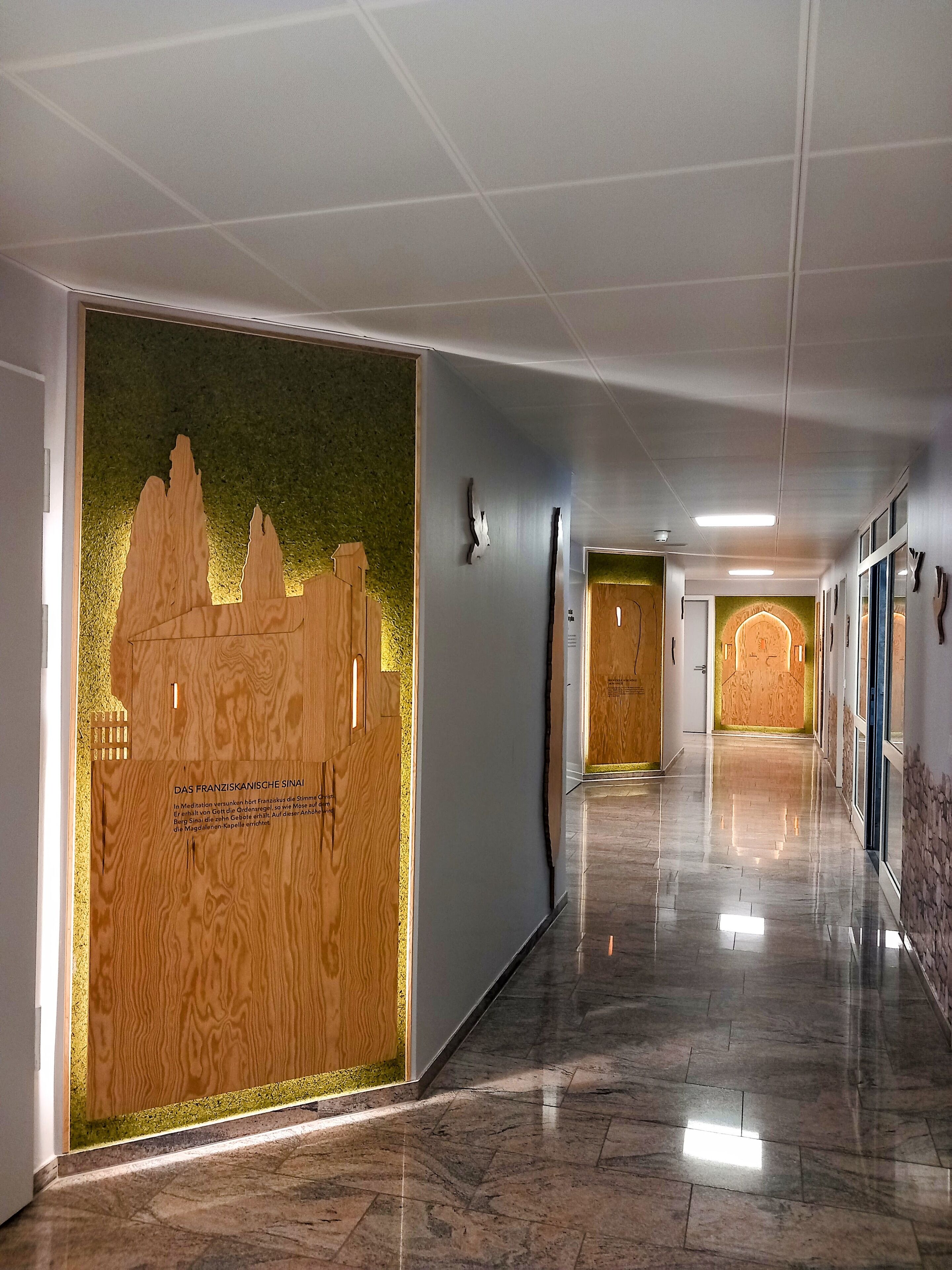 A hallway with a wooden panel featuring a cityscape and text, a polished marble floor, and a series of doors leading to rooms.
