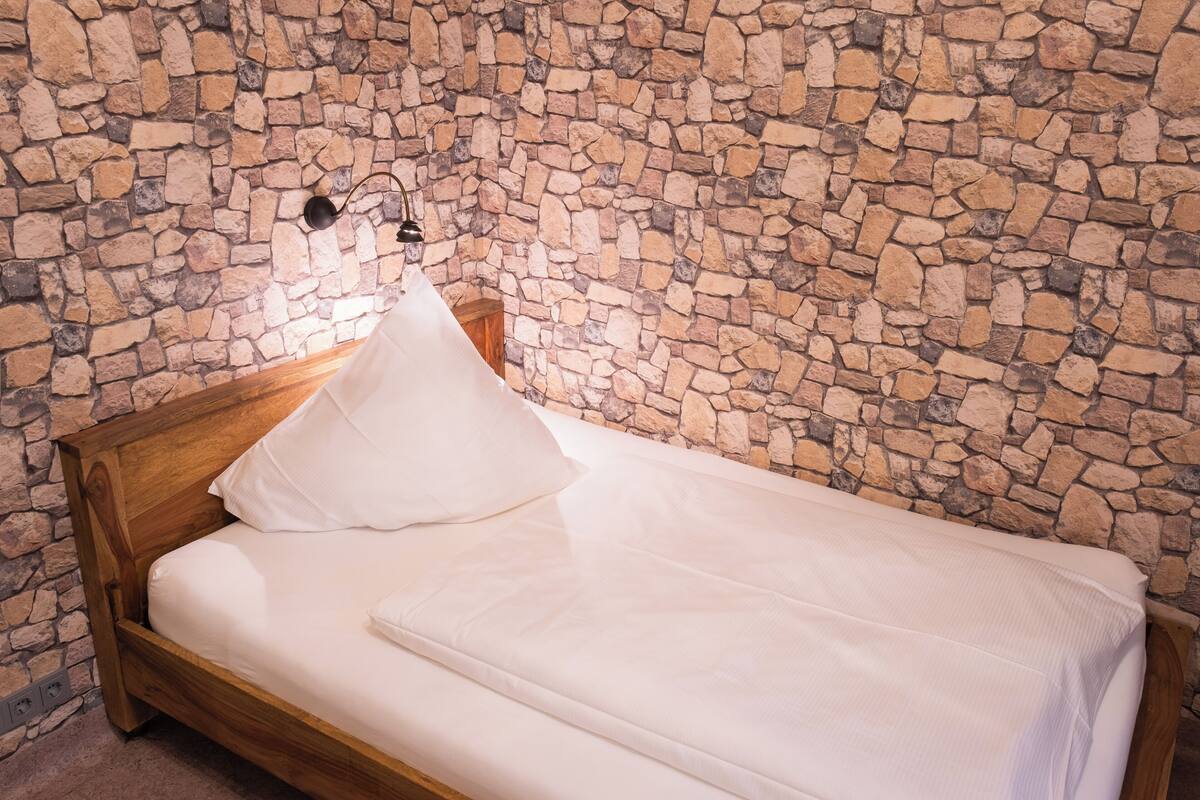 Una cama individual con cabecera de madera en una habitación con pared de piedra.