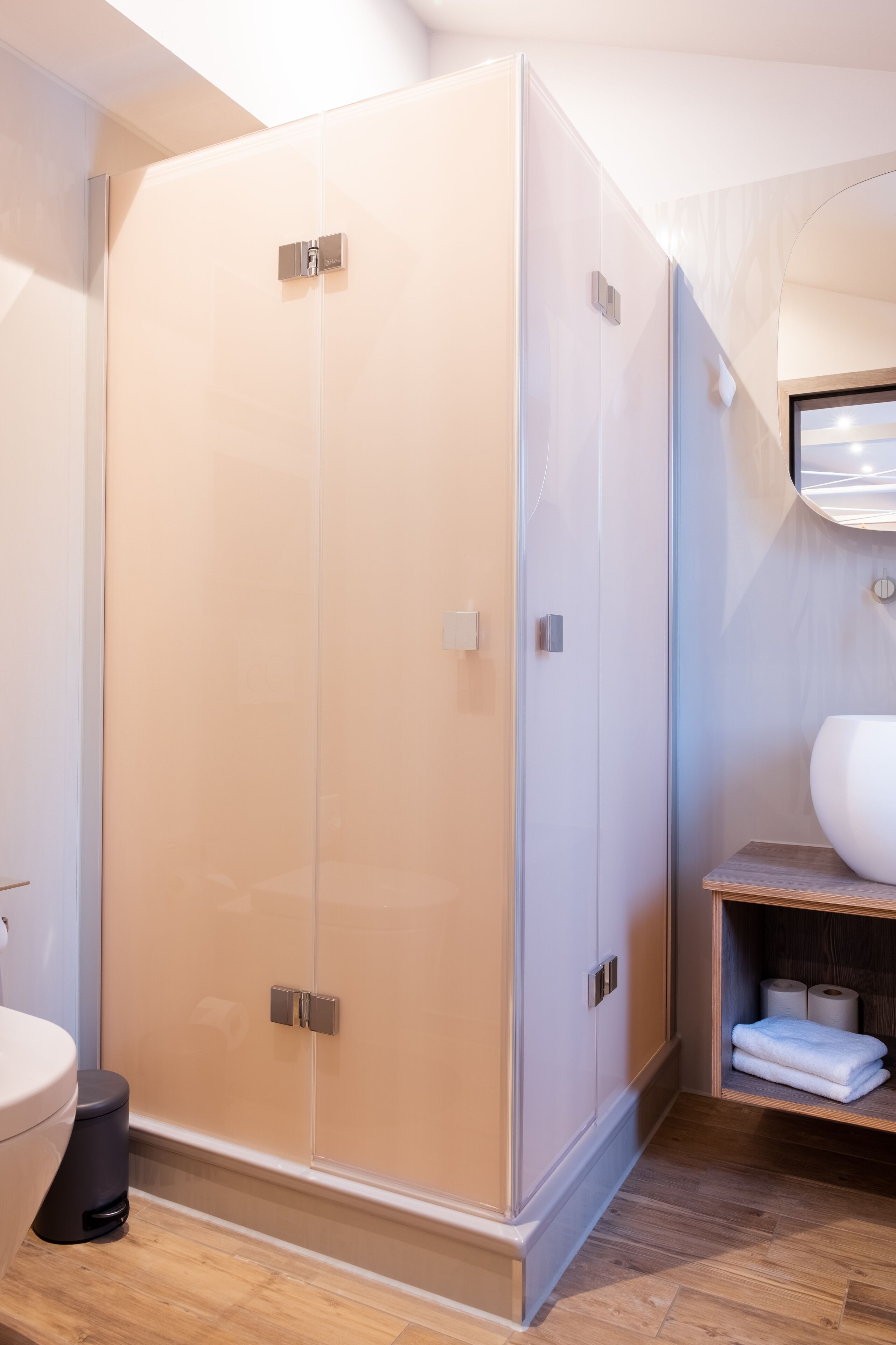 Un baño moderno con ducha envuelta en vidrio, tocador de madera y retrete.