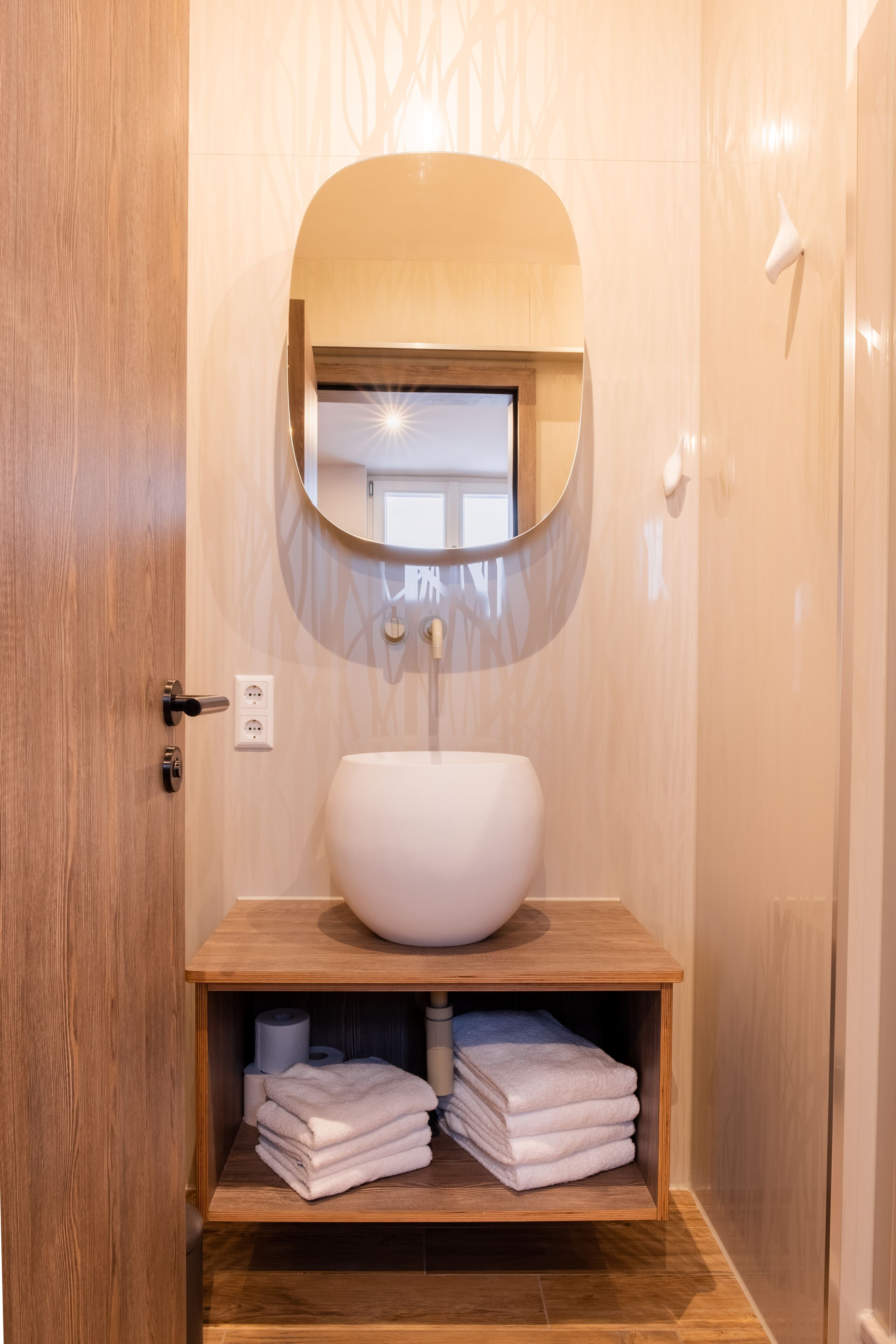 A modern bathroom with a wooden vanity, a round mirror, and neatly stacked towels.