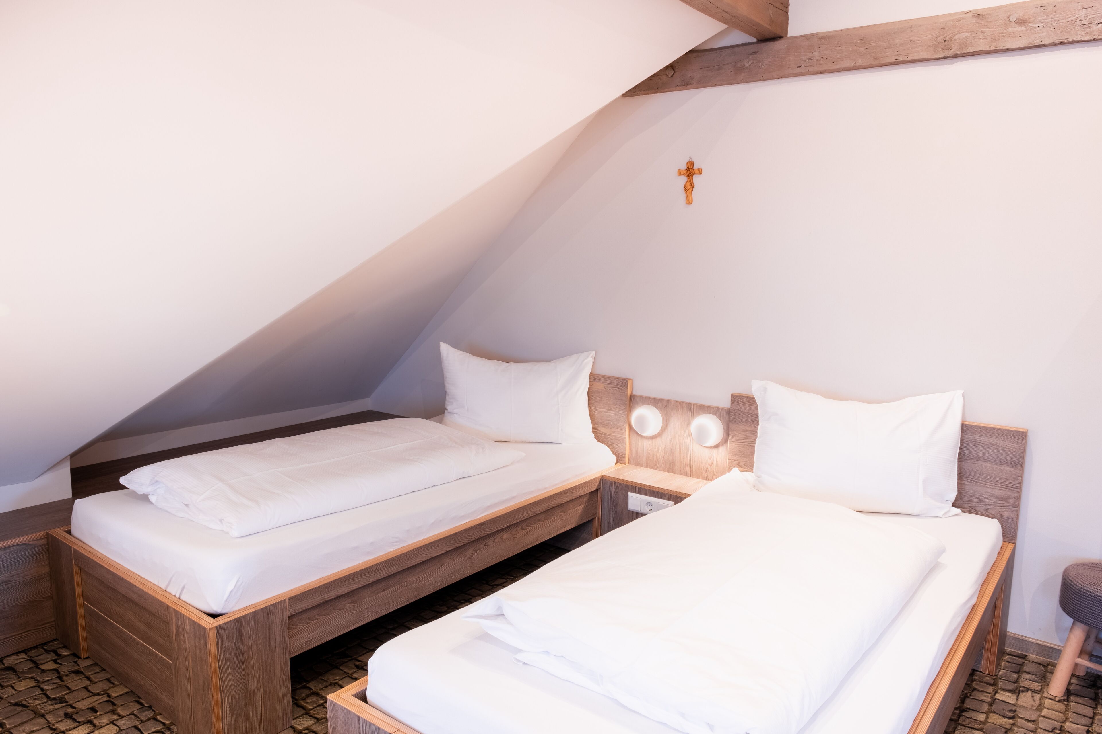 A room with two wooden beds, white bedding, and a cross on the wall.