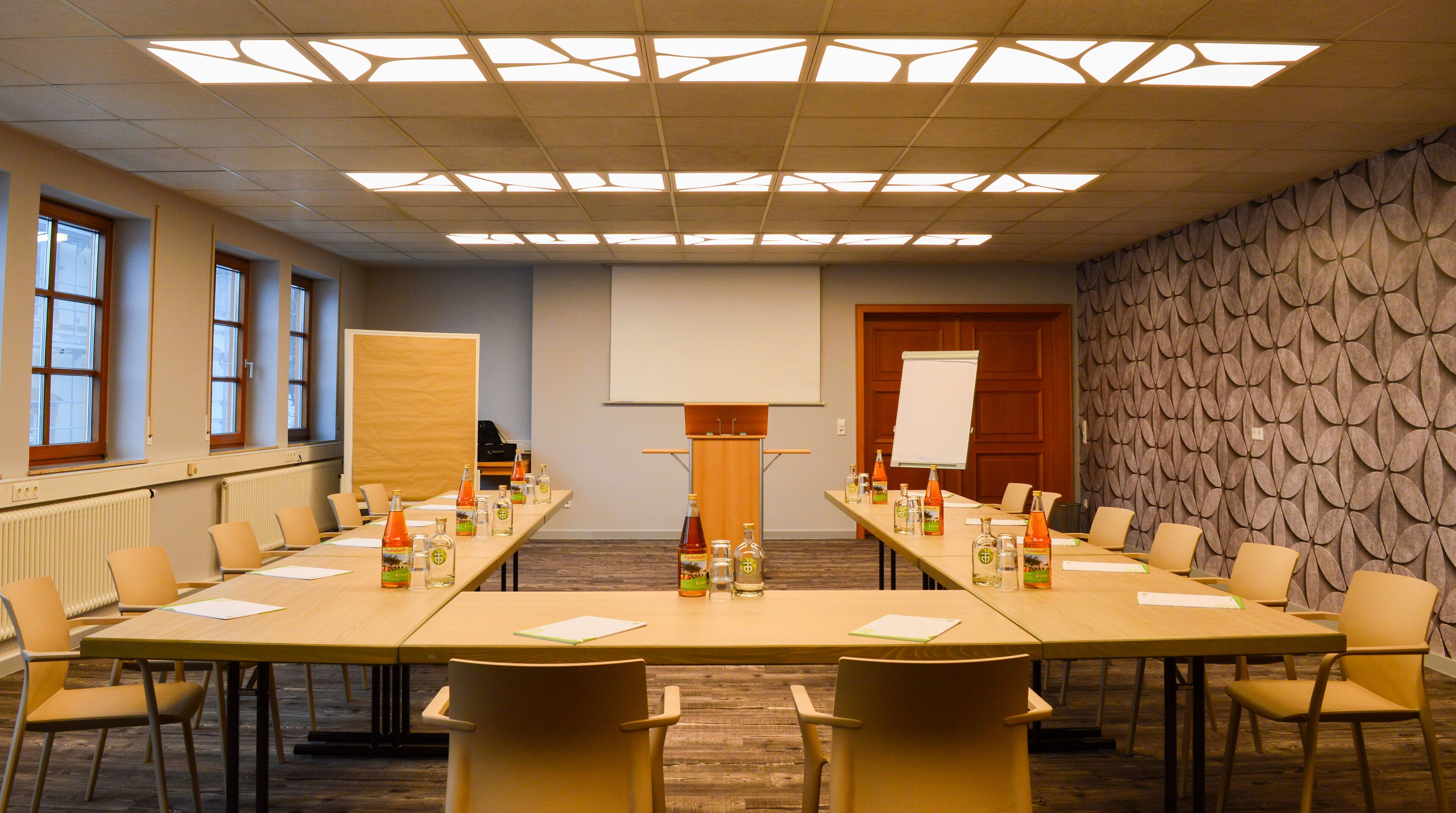 A conference room with a long table, chairs, a whiteboard, and a projector screen.
