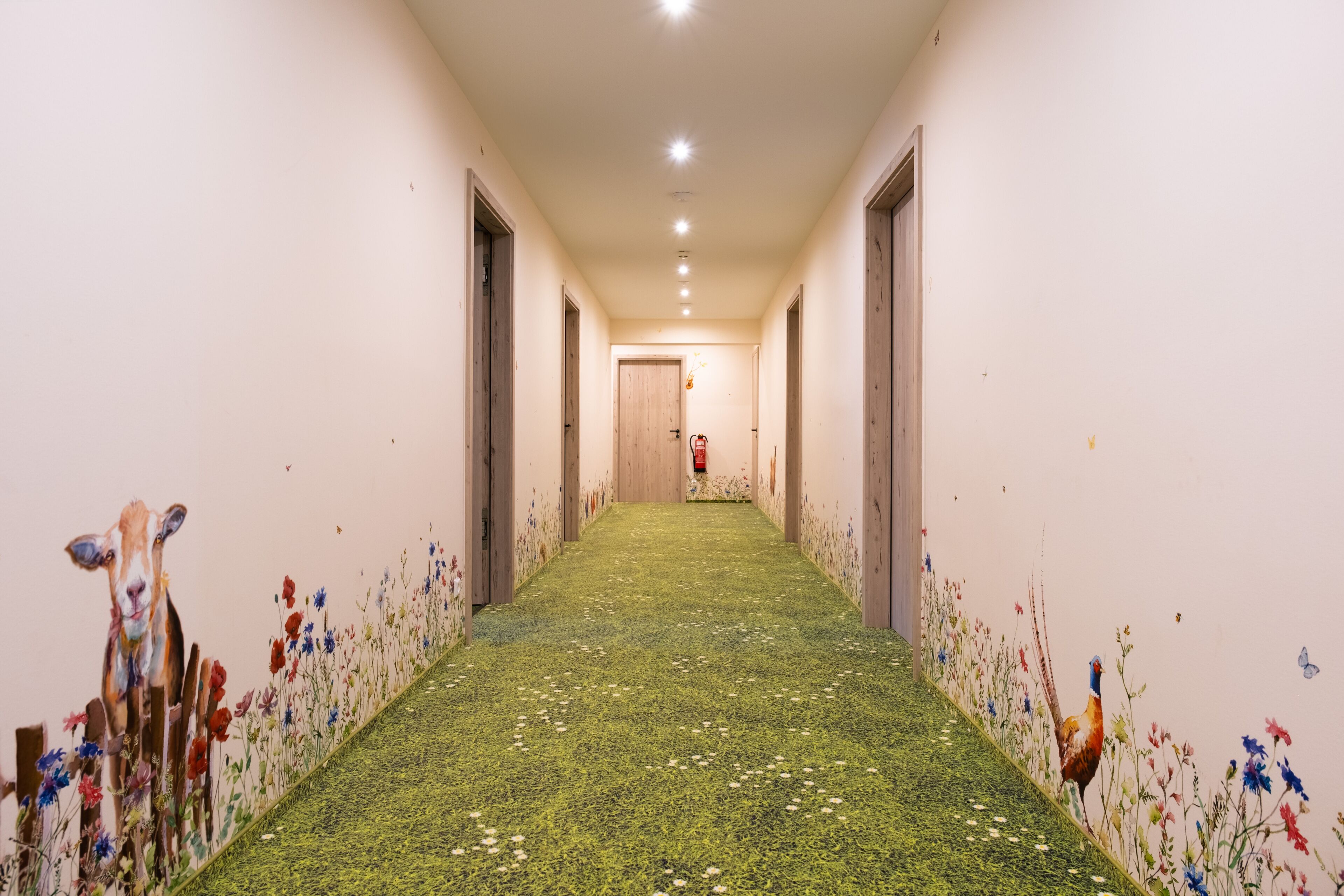 A hallway with a green carpet, wooden doors, and floral wall art.