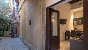 Un edificio residenziale con facciata in pietra, una porta in legno, un patio con piastrelle, un'area pranzo con tavolo e sedie e un televisore montato a parete.