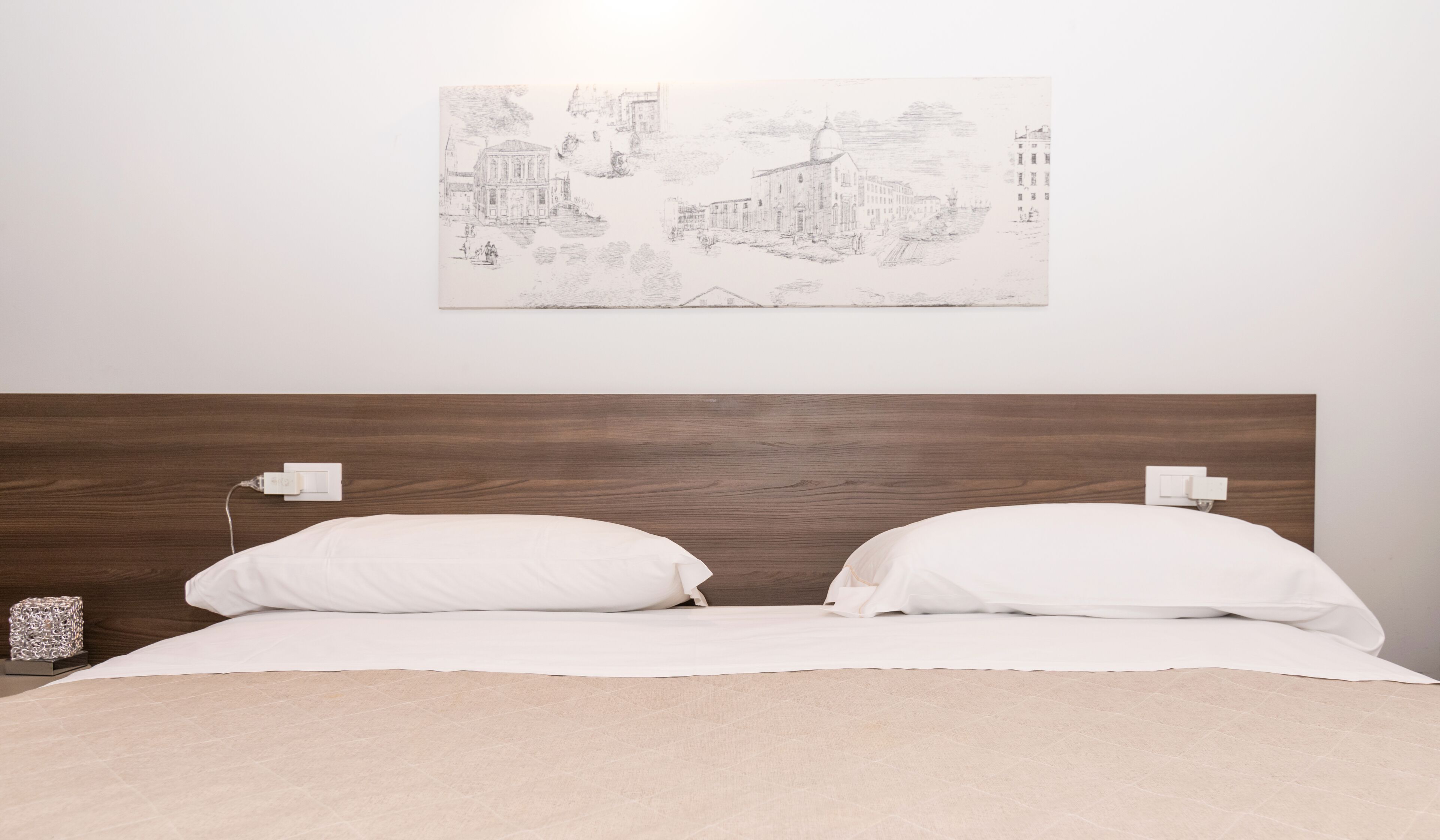 A bedroom with a wooden headboard, white bedding, and a wall-mounted light fixture.