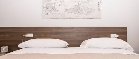 A bedroom with a wooden headboard, white bedding, and a wall-mounted light fixture.