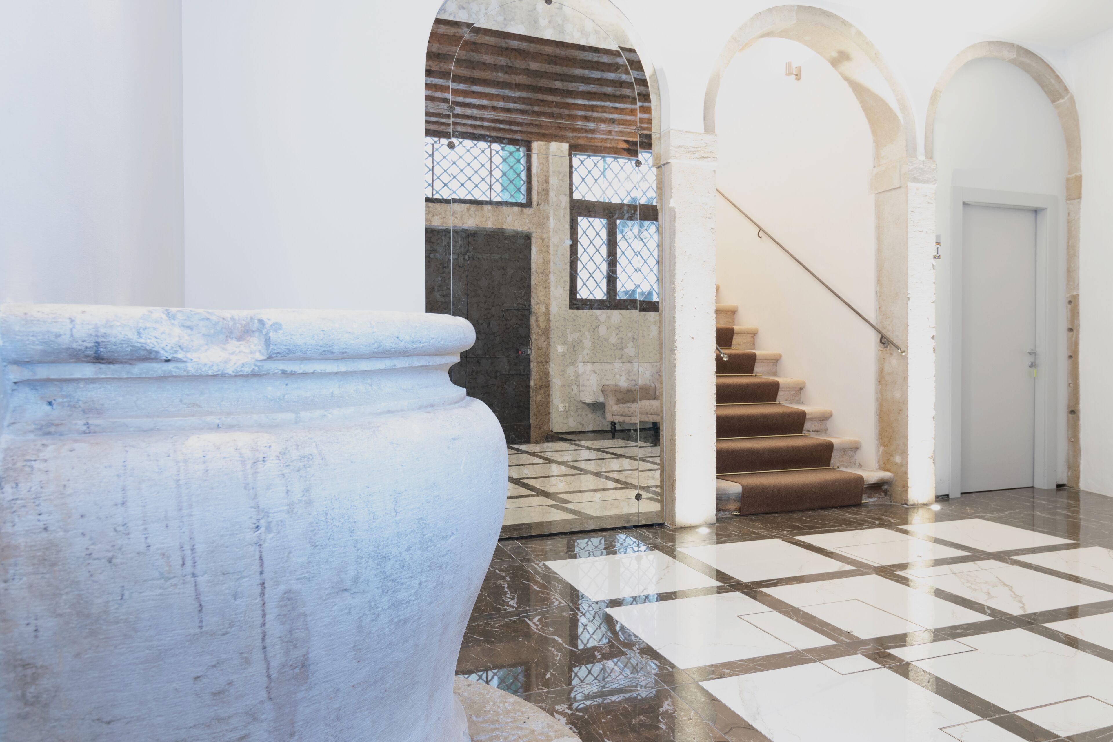 A spacious lobby with a large stone column, a staircase with brown steps, and a tiled floor.