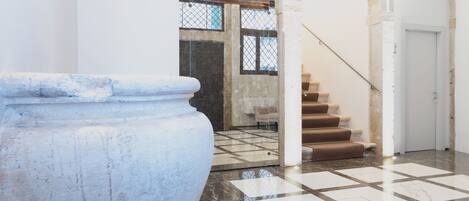 A spacious lobby with a large stone column, a staircase with brown steps, and a tiled floor.