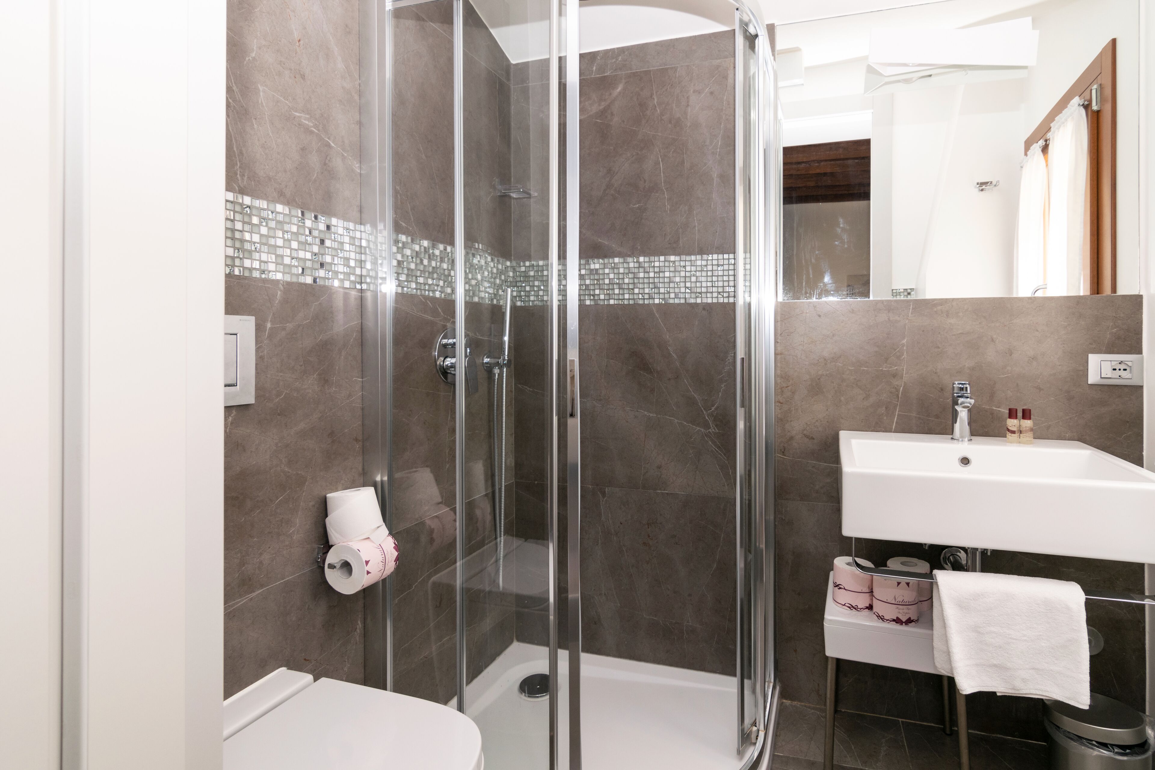 A modern bathroom with a glass-enclosed shower, a white sink, and a toilet.