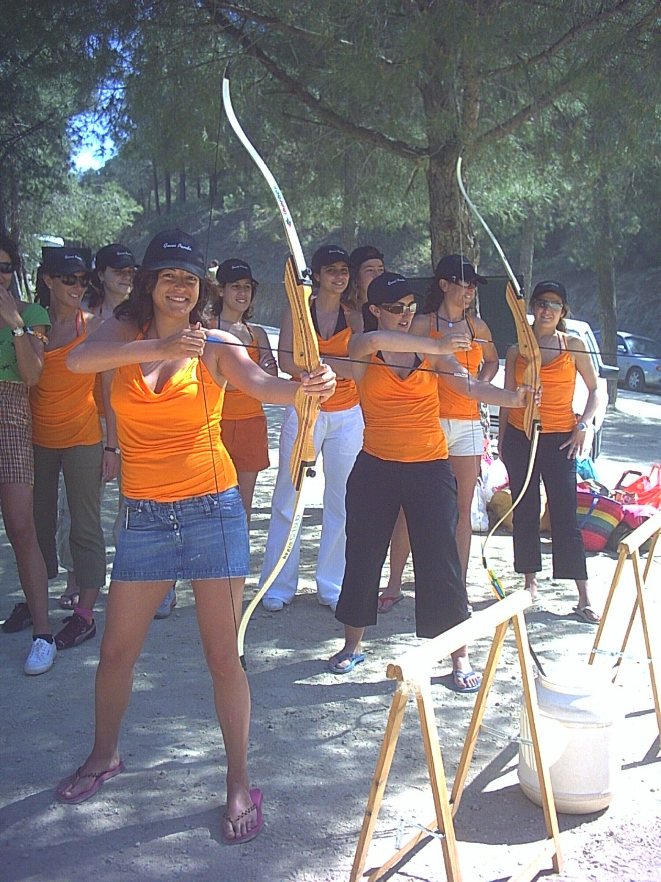 Un grupo de personas con camisetas anaranjadas practicando tiro con arco al aire libre.