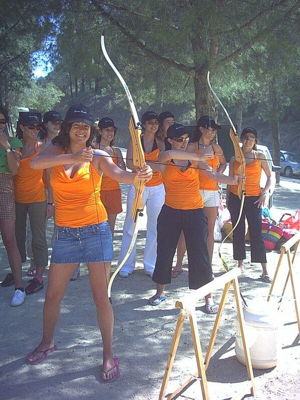 A group of people in orange shirts practicing archery outdoors.