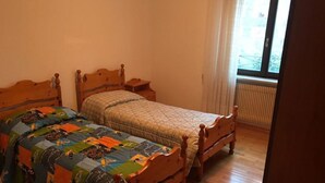 Ein Schlafzimmer mit zwei hölzernen Betten, einem Fenster mit Vorhängen und einer Heizung.