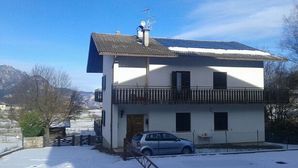 Ein zweistöckiges Haus mit Balkon, ein Auto davor und eine verschneite Landschaft im Hintergrund.