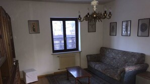Ein Wohnzimmer mit gepolstertem Sofa, einem Holztisch, einer Heizung, einem Fenster mit Aussicht und einer Chandelier.