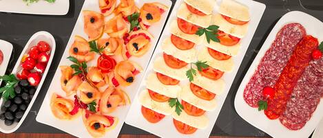 Uma mesa com diversos alimentos, incluindo tomates fatiados, queijo e embutidos.