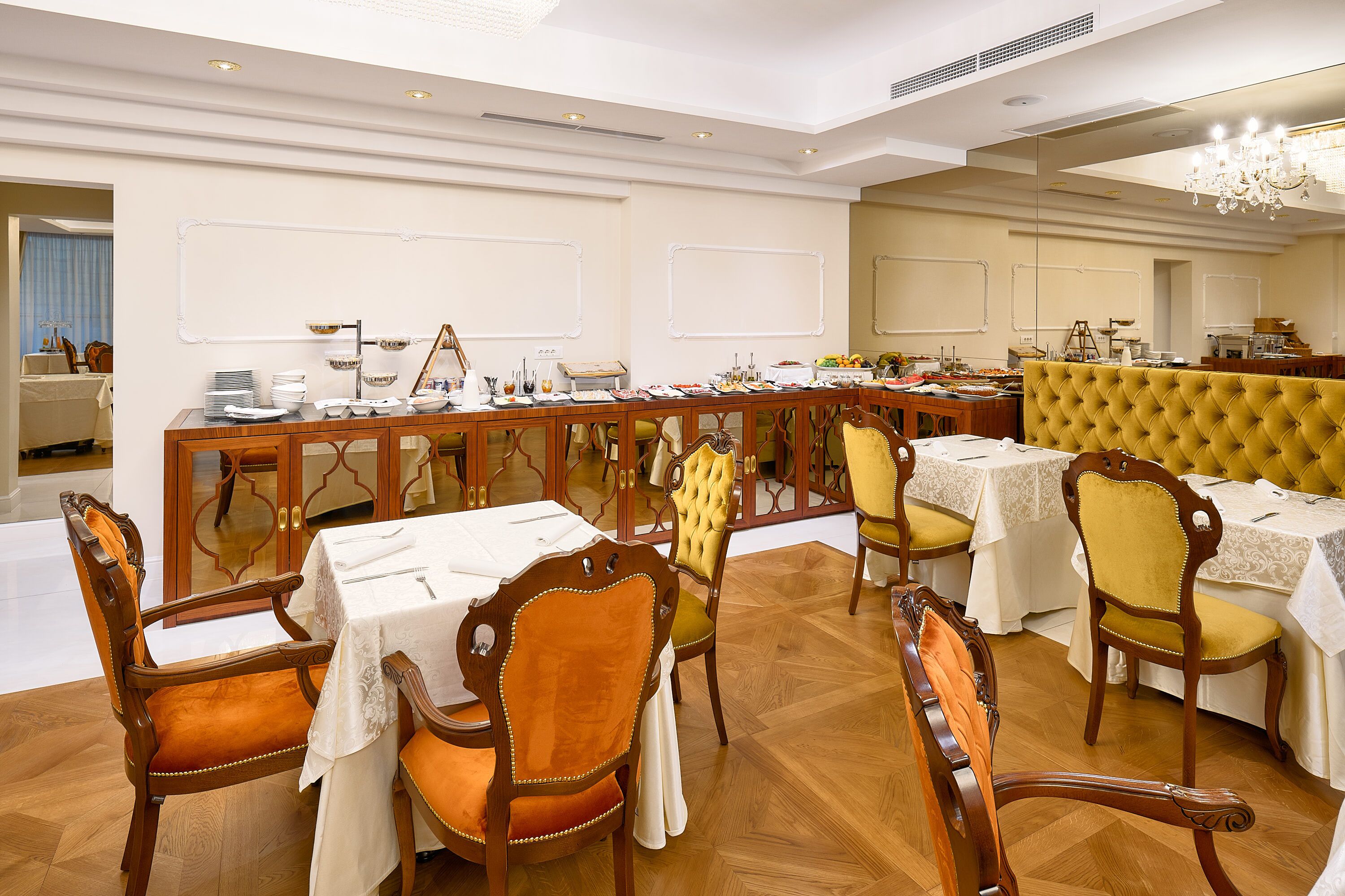A dining area with wooden chairs and tables, a buffet setup, and a mirror reflecting the room.
