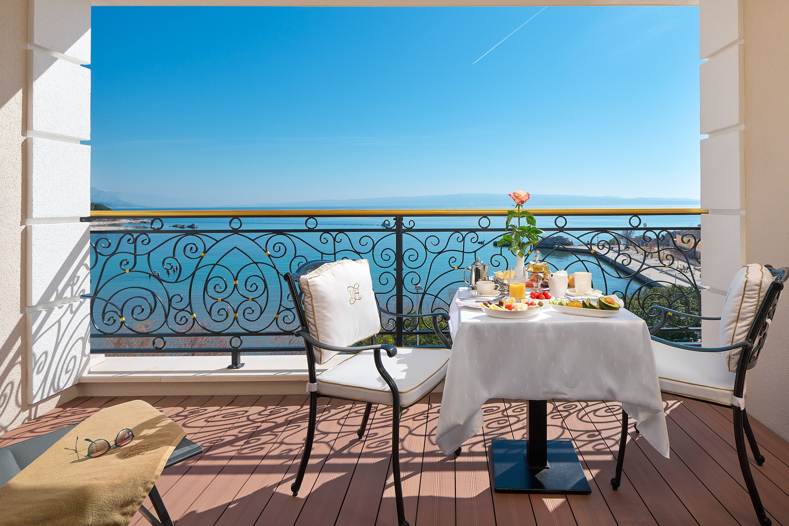 A balcony with a table set for breakfast, a chair, and a view of the sea.