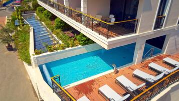 A rooftop swimming pool with sun loungers and a balcony with a railing.
